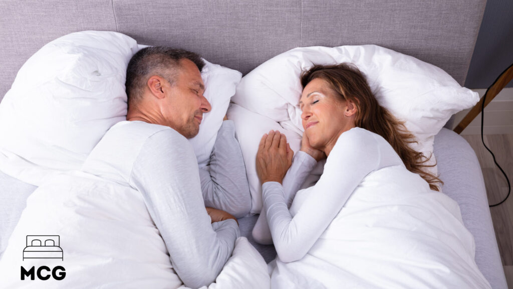 couple sleeping together in a bed with white sheets