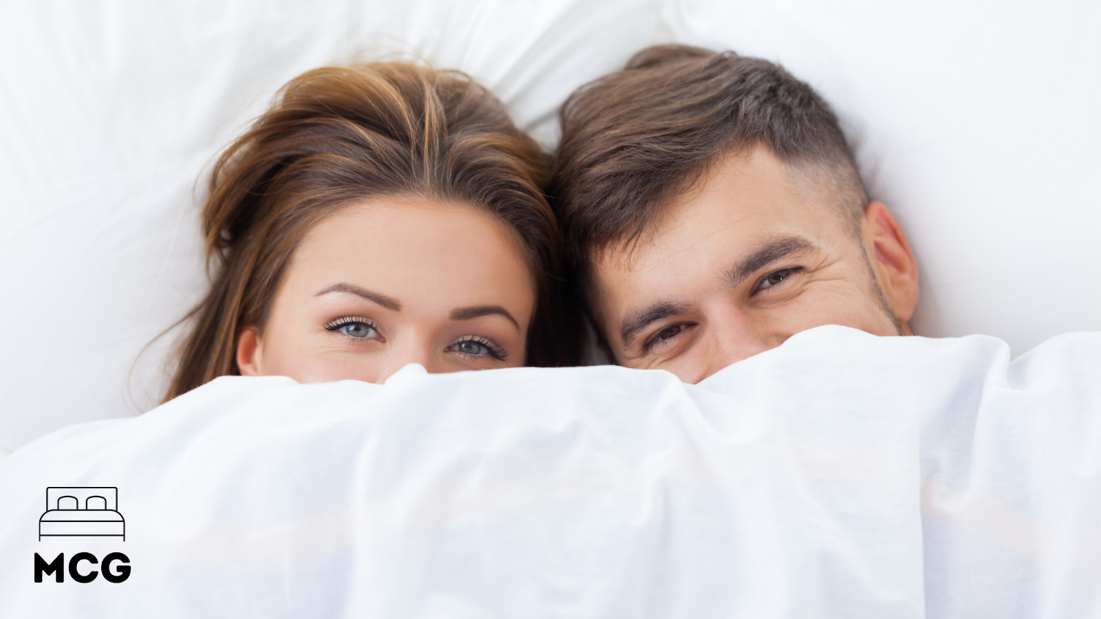 man and woman in bed looking out from beneath a sheet